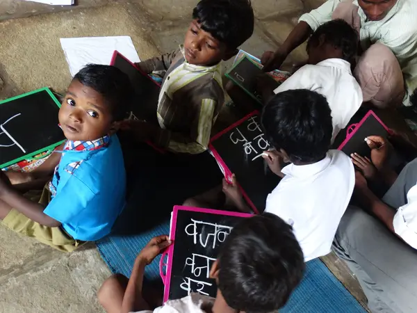 Children sitting on a mat on the floor writing on small chalk slates