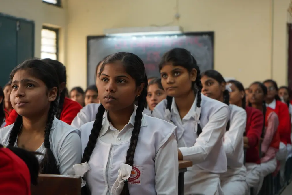 Girls in school uniforms with braided hair sitting in rows in a classroom