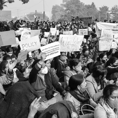 Black and white photo of a seated crowd holding handwritten signs reading We Want Policy at a protest