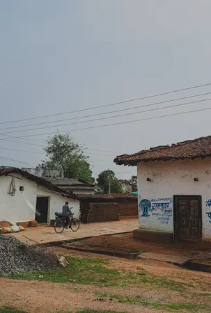 Village lane with whitewashed tiled-roof houses, a man on a bicycle and power lines under a grey sky