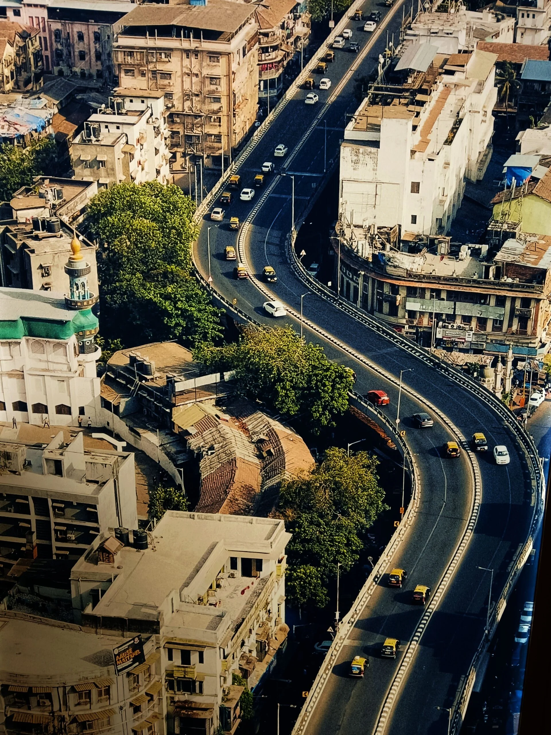 Aerial view of a curved flyover with taxis and cars passing old city buildings and trees