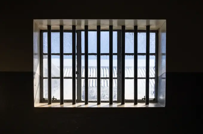 Barred window in a dark prison wall letting in daylight