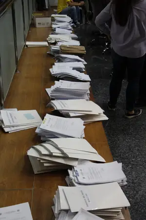 Long wooden counter covered with stacks of paper files and forms, with a person standing nearby