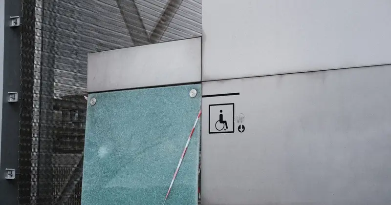 Wheelchair accessibility sign on a grey wall beside a cracked glass panel with red and white tape