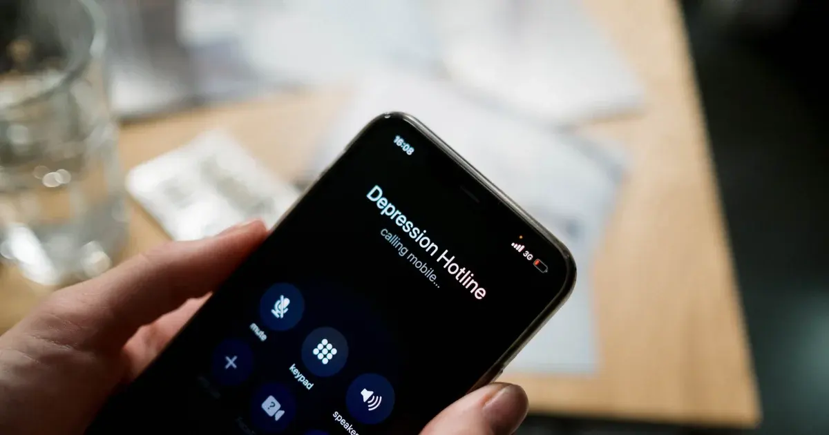 Hand holding a smartphone screen showing a call to a depression hotline, with the call connecting