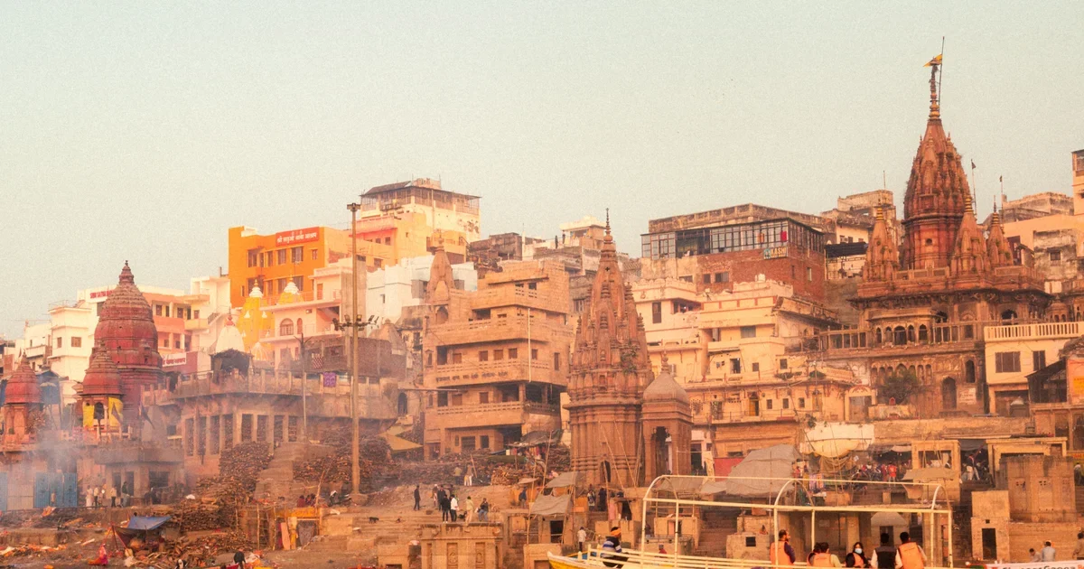 Riverside ghats with temple spires and multicoloured buildings in hazy light