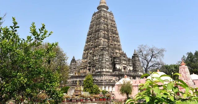 Mahabodhi Temple tower in Bodh Gaya seen through green foliage under a clear blue sky
