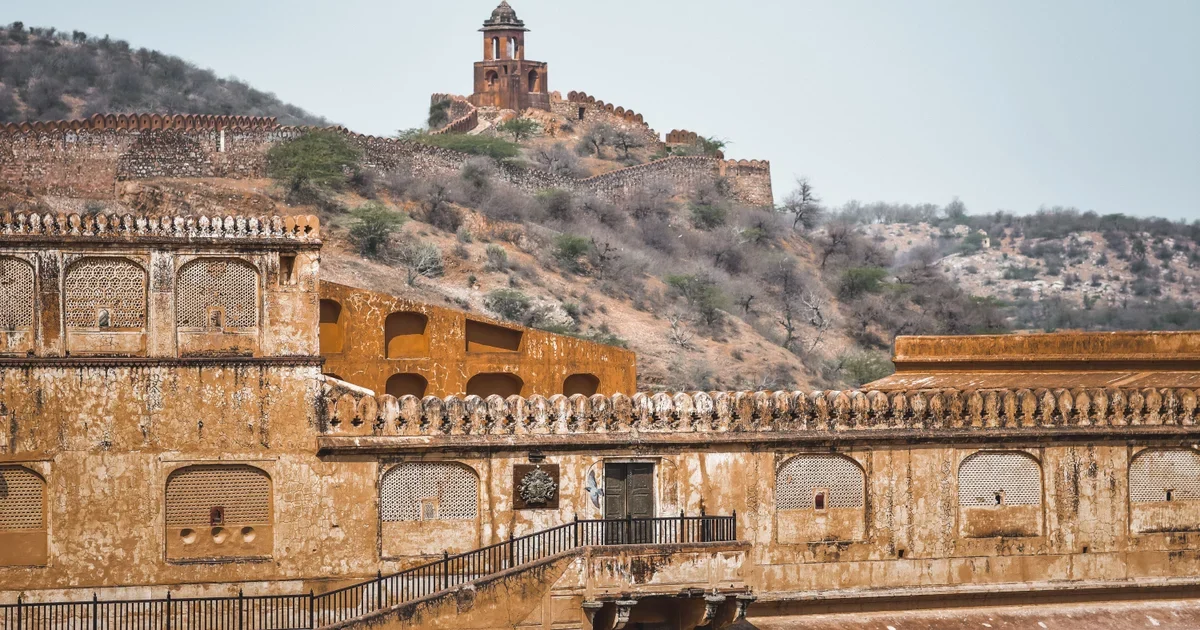 Sandstone palace walls with jali windows below a hilltop watchtower and fort wall
