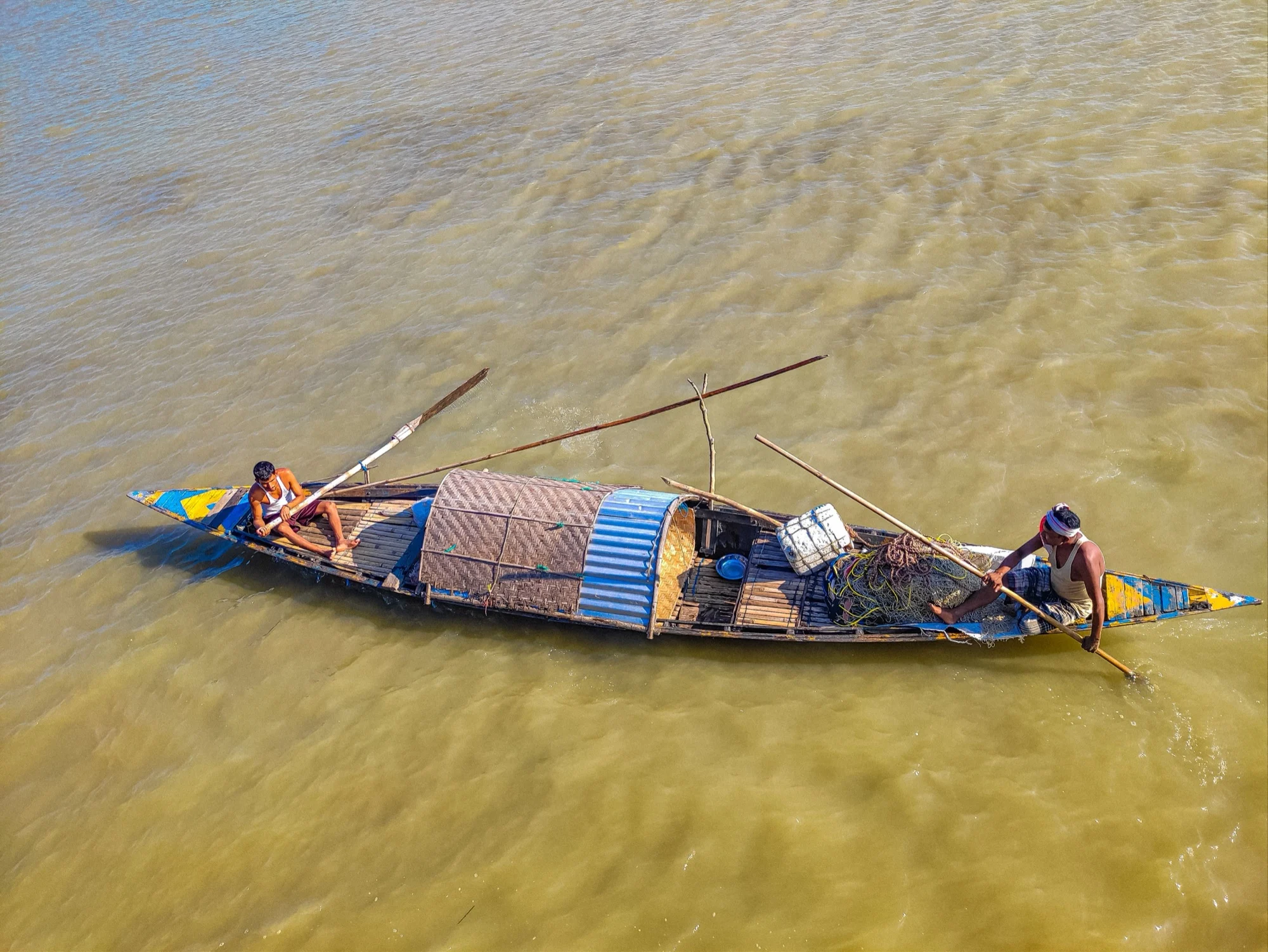 Fishermen steering a wooden boat across the wide Brahmaputra River in Assam