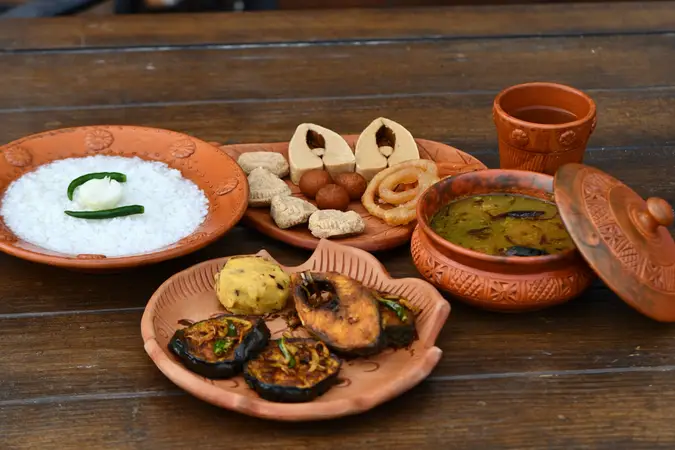 Bengali meal of rice, fried fish, dal, begun bhaja and sweets served in clay dishes
