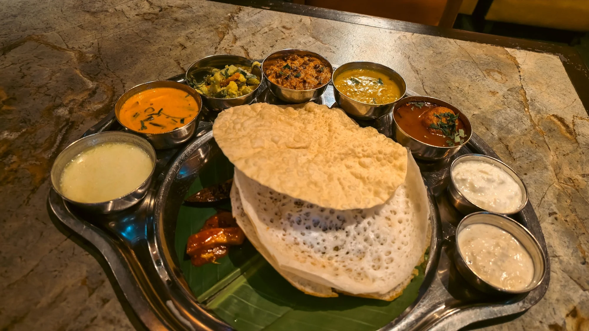 Kerala-style thali with a lacy appam and coconut curries in steel bowls