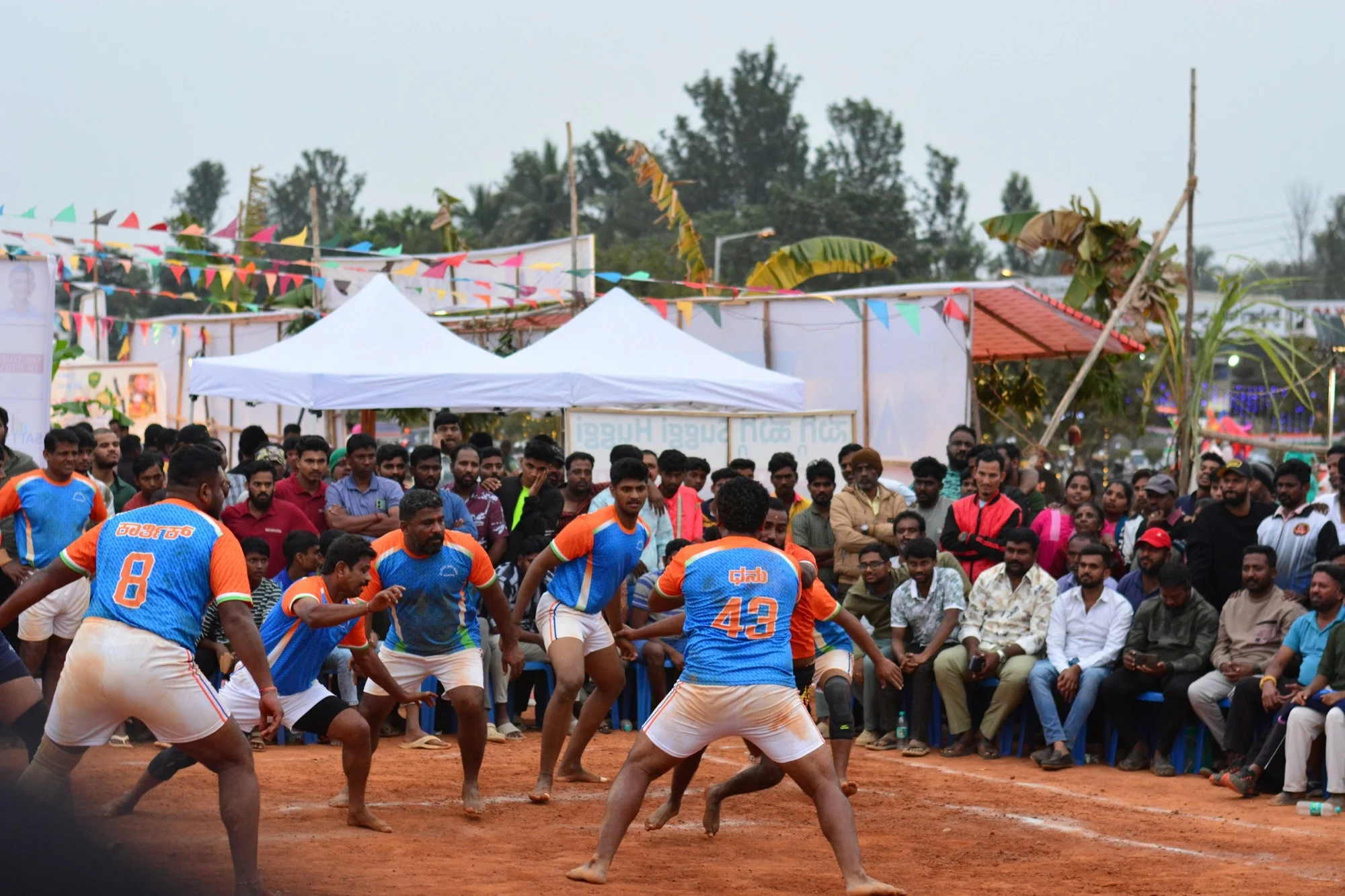 Kabaddi raiders and defenders mid-match on a mud court as a crowd watches