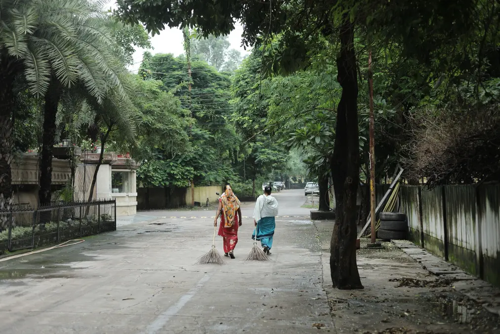 Two women sanitation workers sweeping a tree-lined street in Raipur