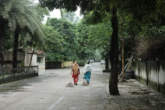 Two women sanitation workers sweeping a tree-lined street in Raipur