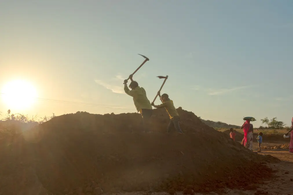 Rural workers digging earth with pickaxes at sundown in an Indian village