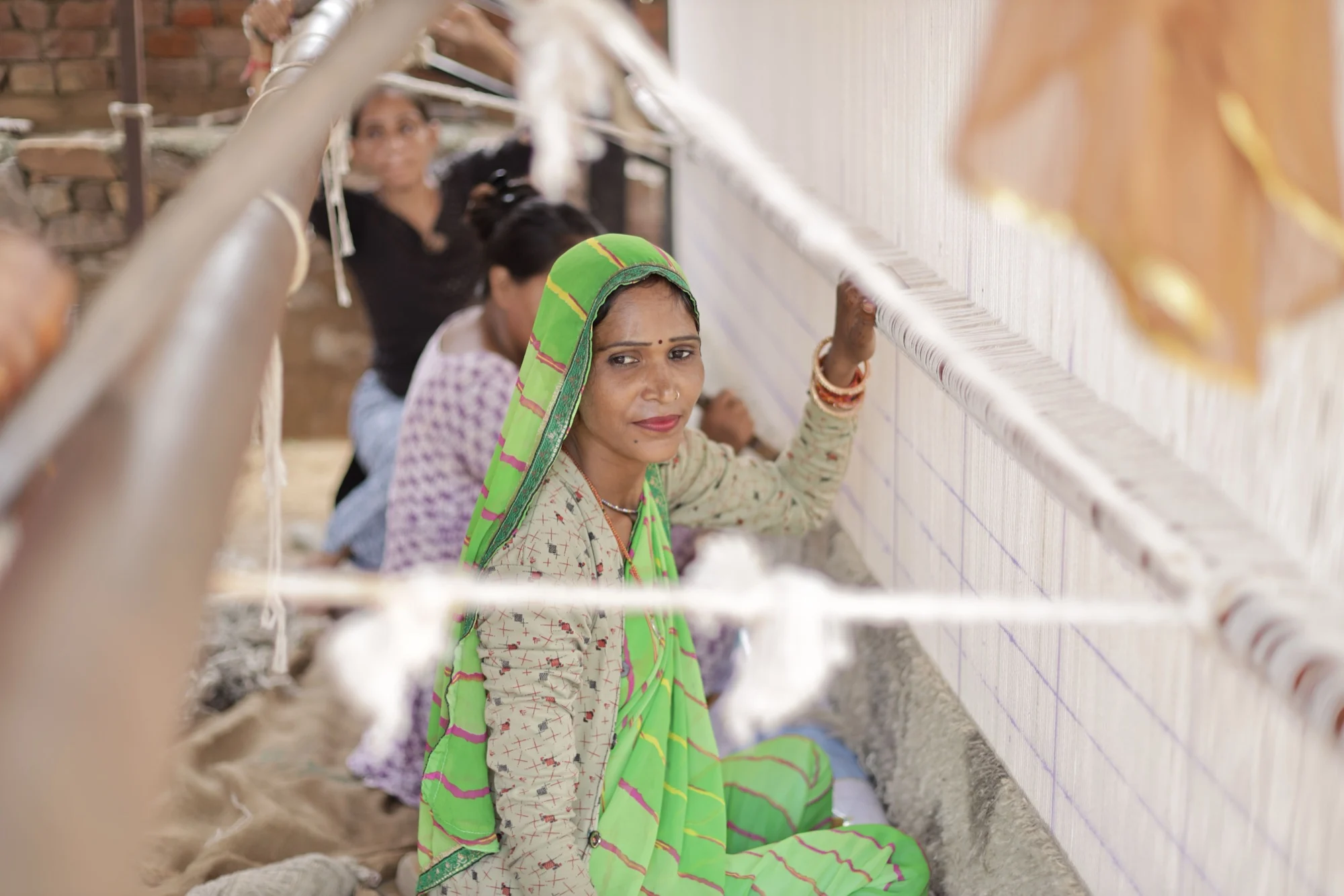 Woman in a green sari working threads on a traditional hand loom