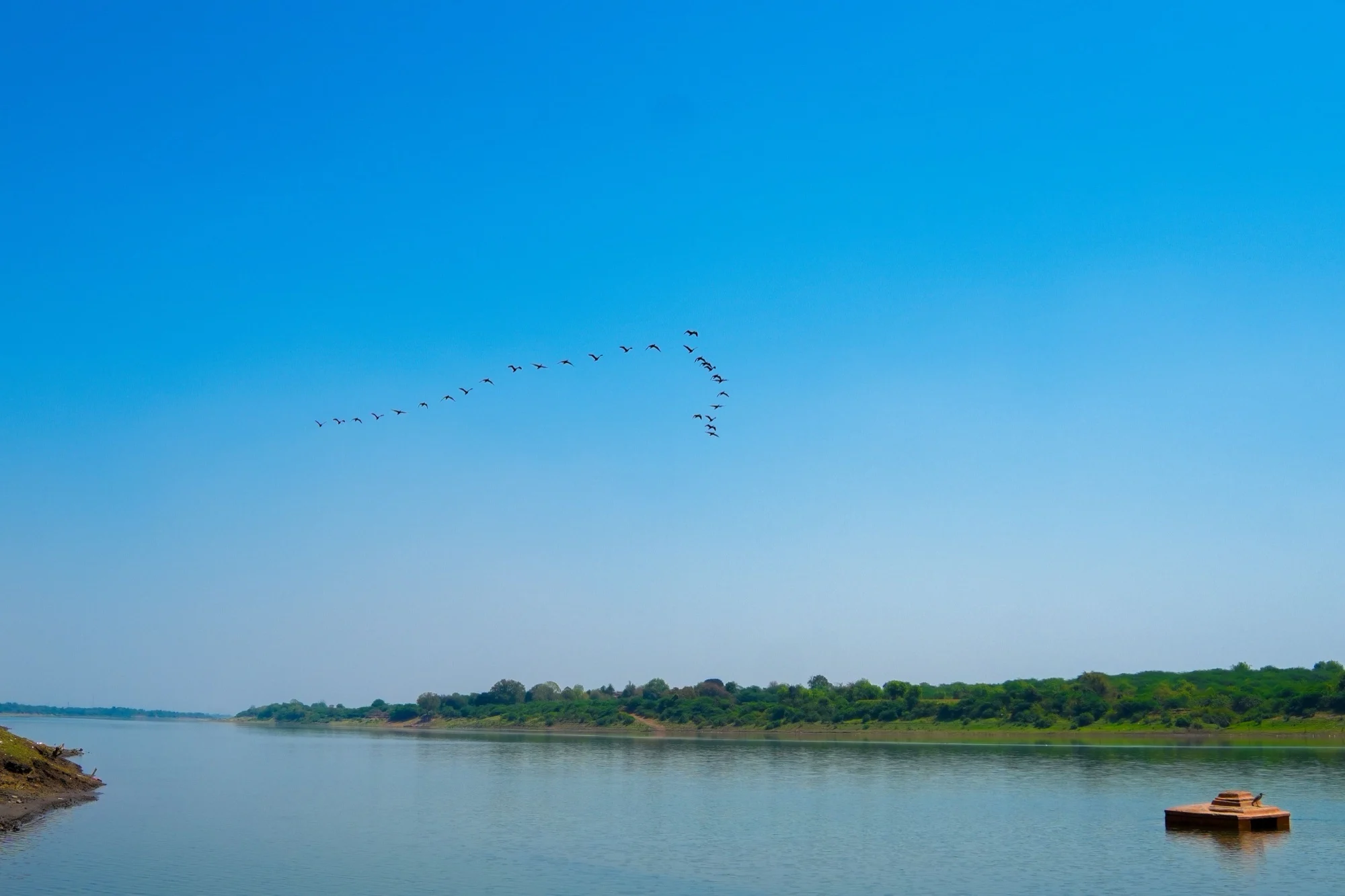 The Narmada River at Dharampuri with a line of birds crossing a clear sky