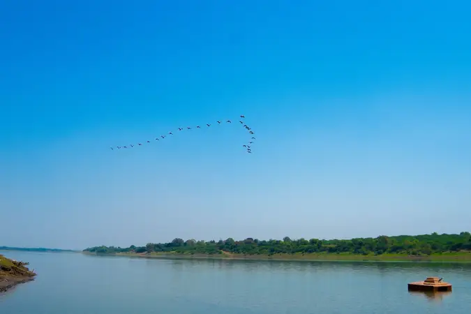 The Narmada River at Dharampuri with a line of birds crossing a clear sky
