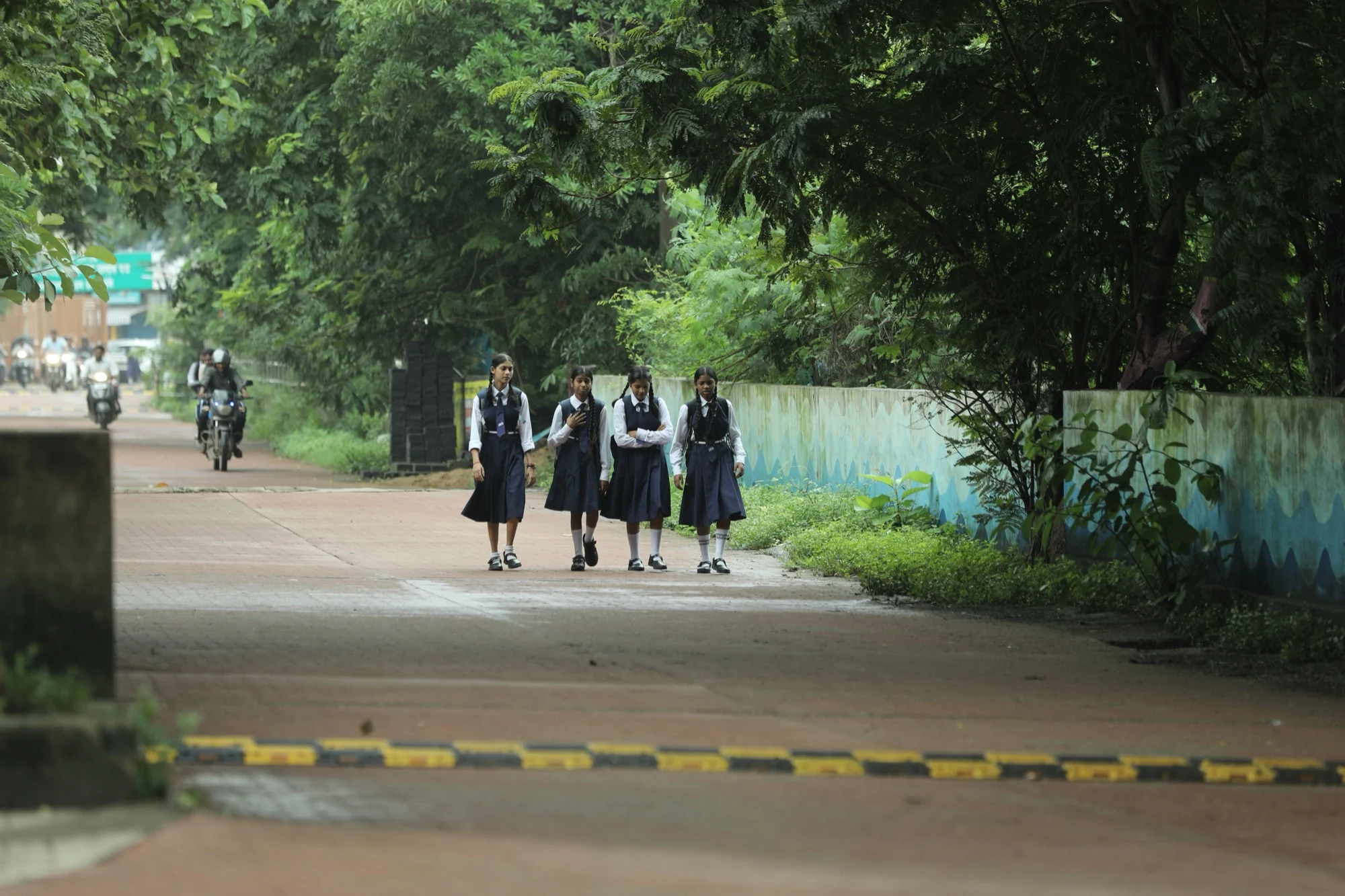 Four schoolgirls in uniform walking together down a tree-lined road in Raipur