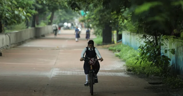 A schoolgirl in uniform rides a bicycle along a green pathway in Raipur, India