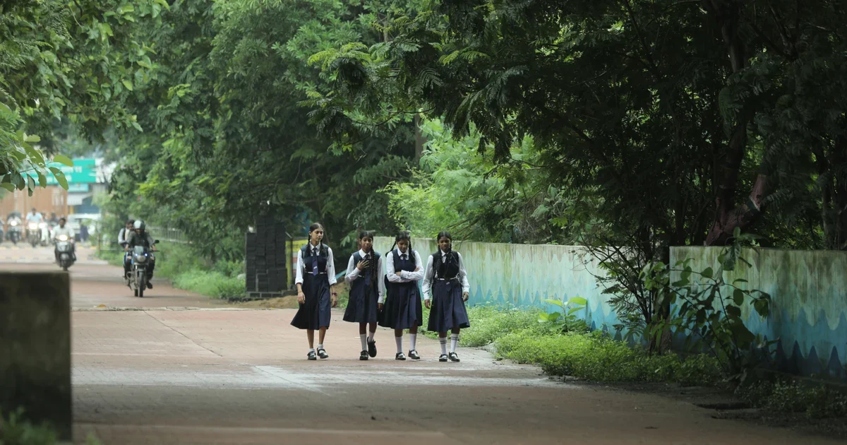 Four schoolgirls in uniform walking together along a tree-lined path in Raipur, India
