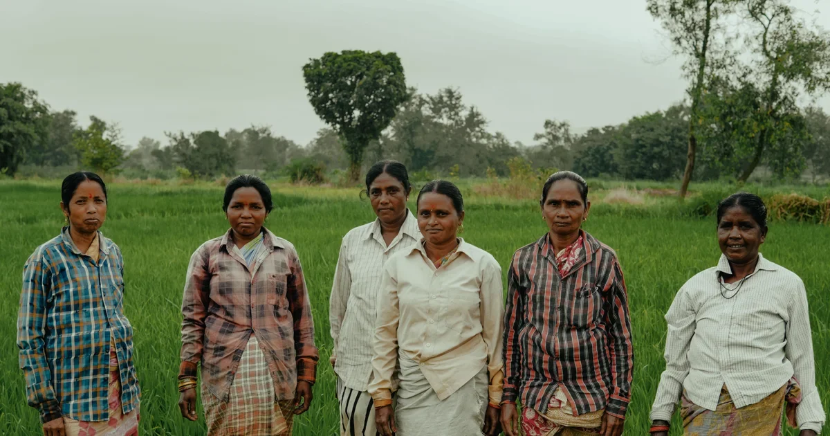 Five women stand together in a green field in rural India