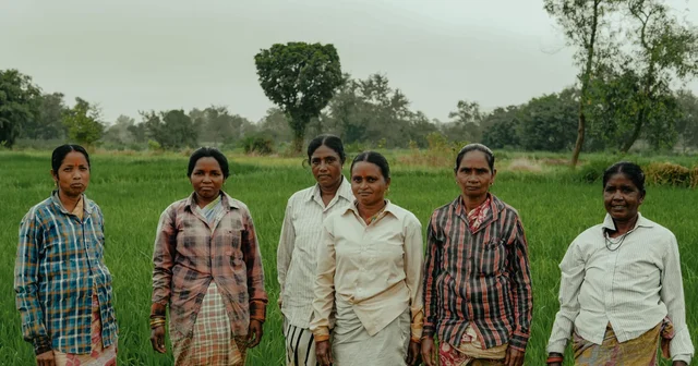Five women stand together in a green field in rural India