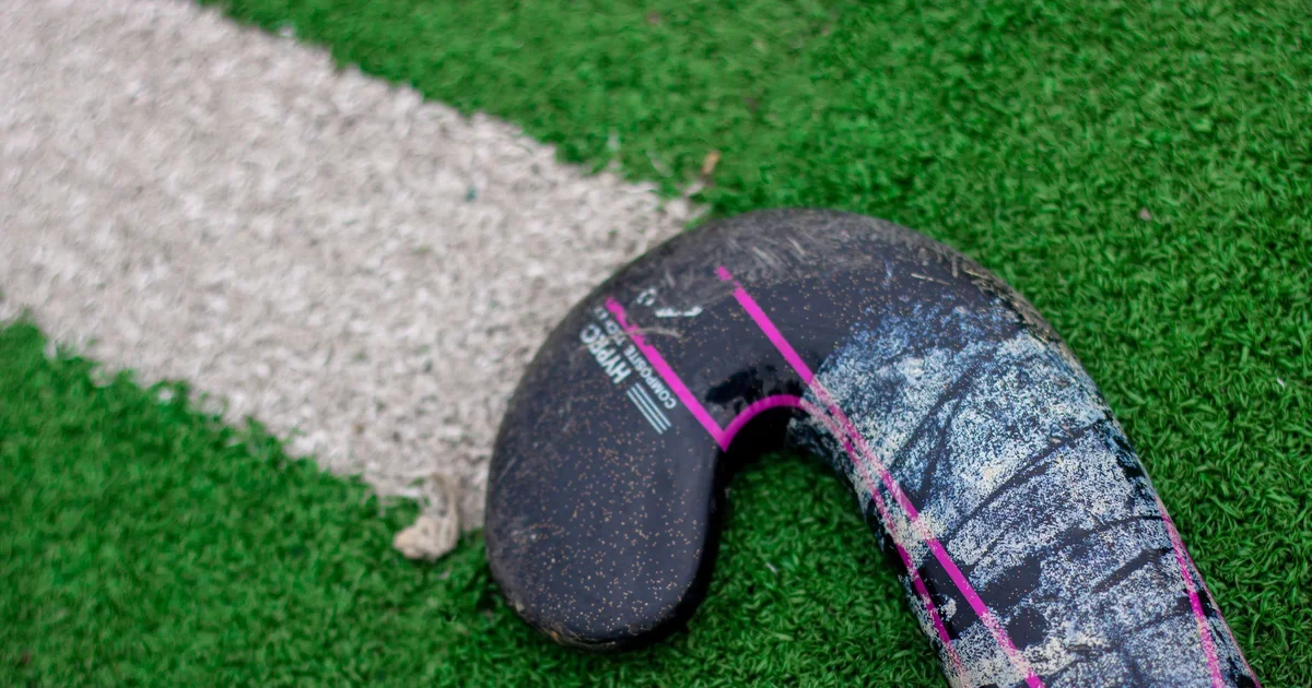 A field hockey stick lying on a green artificial turf pitch