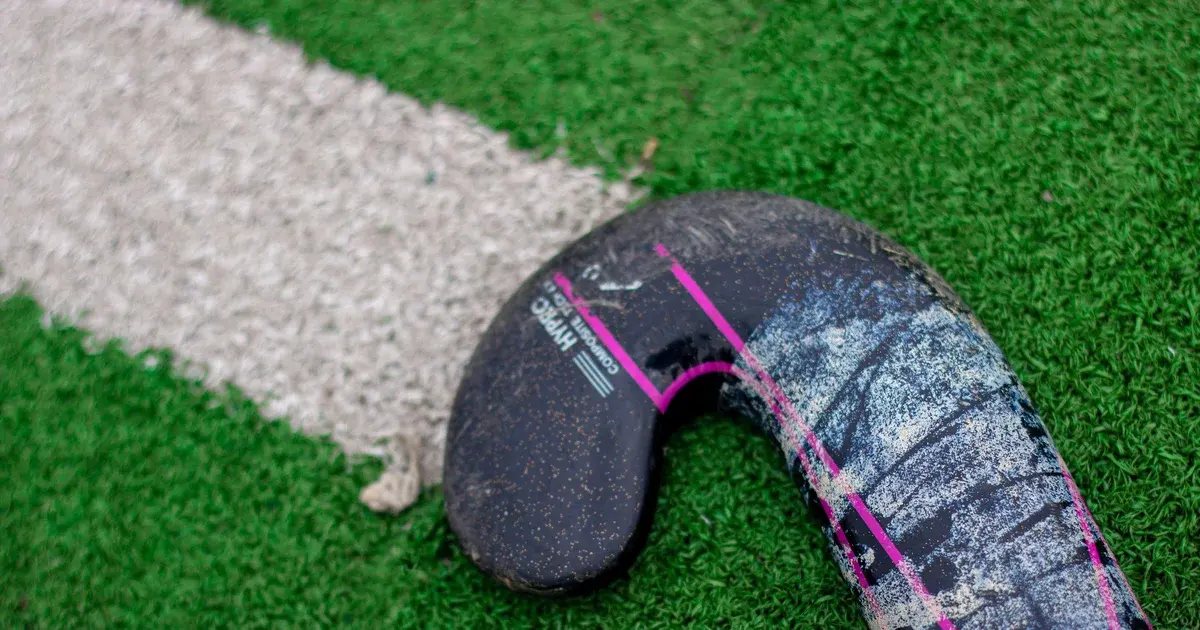 A field hockey stick lying on a green artificial turf pitch